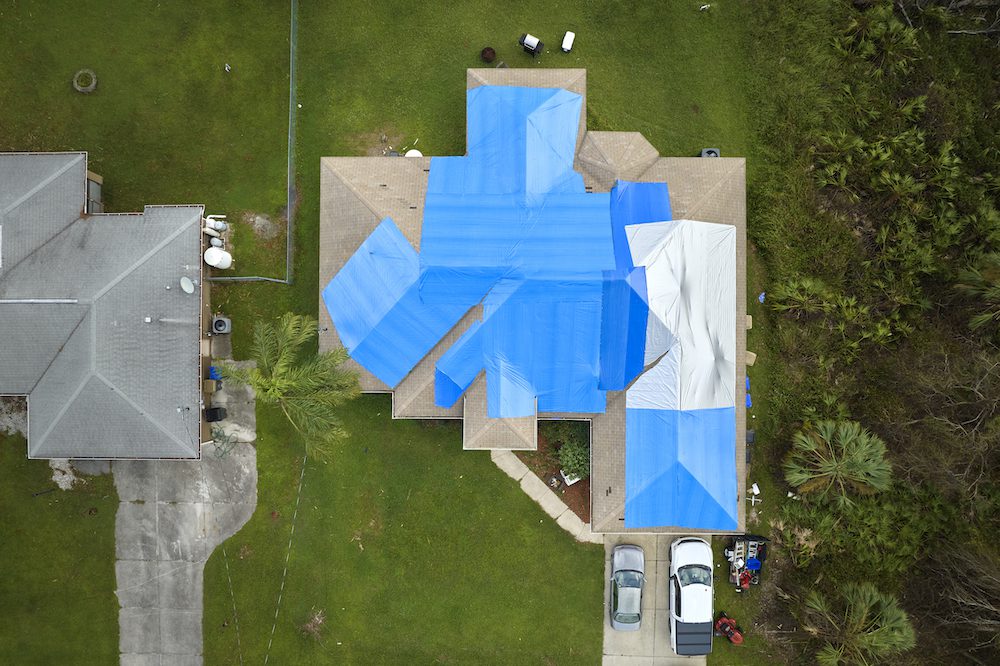 drone view of a house with cars in the driveway surrounded by green lawn covered with blue protective plastic tarp after hurricane Ian
